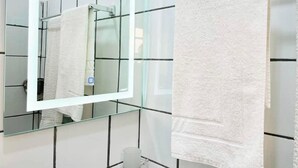A bathroom with a white tiled wall, a glass-topped sink, and a white towel hanging on a rack. - 1 Bed Studio Sleeps 2 - Wifi, Balcony, Parking (Douala)