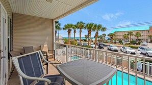 A balcony with a pool view, outdoor seating, and a view of the beach and ocean.