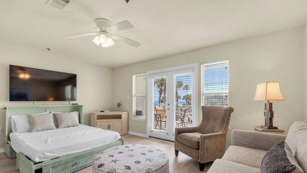 A hotel room with a bed, a chair, a small table, a lamp, and a ceiling fan.