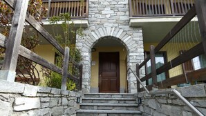 Un escalier en pierre menant à une porte, de part et d’autre de laquelle se trouve une rambarde en bois.