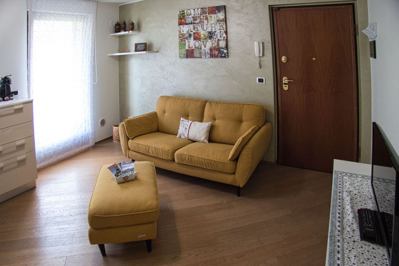 Olohuone, jossa on sohva ja rahi, puuovi sekä seinä, jossa on koristeellinen kyltti, jossa lukee: ”HOME NATURE LOVE”.
