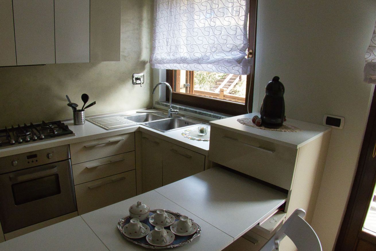 A compact kitchen with a gas stove, oven, sink, and a window with a curtain.