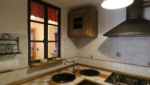 Una cocina con dos fregaderos, una estufa, un ventanal con cortinas y una lámpara colgante.