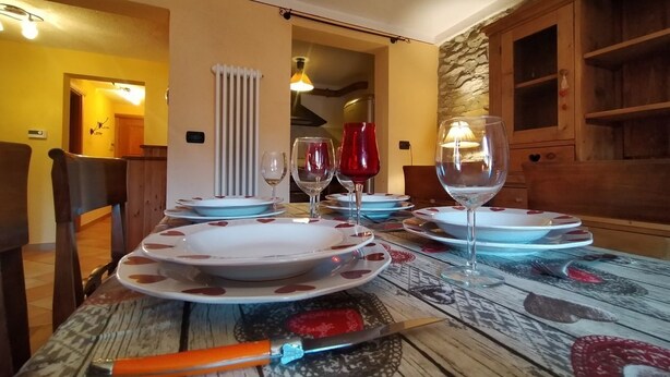 Una mesa de comedor preparada con platos, vasos y cubiertos en una habitación con muebles de madera y pared de piedra.