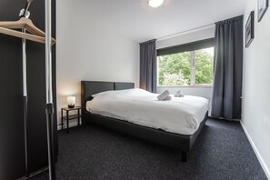 Une chambre à coucher avec un lit, une table de chevet avec une lampe, une armoire et une fenêtre avec des rideaux.