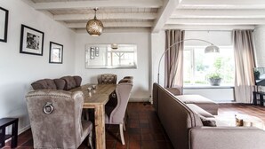 A dining area with a wooden table and cushioned chairs, a sofa, and a large window with curtains.