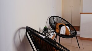 Ein kleiner, abgeschlossener Raum mit zwei schwarzen Metallstühlen, einem Tisch mit einer Pflanze und einer Tür mit Milchglasfenster.