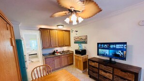 Una cocina compacta con armarios de madera, una mesa de comedor y un televisor montado en la pared.