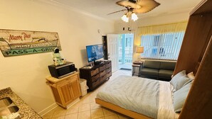 Un dormitorio con cama, televisión, microondas, armario de madera, lavabo y ventana con cortinas.