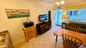 Un comedor con una mesa y sillas de madera, un televisor sobre un mueble bajo, una cafetera y un letrero en la pared.