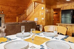A dining area with a wooden table set for four, a staircase, and a kitchen area.