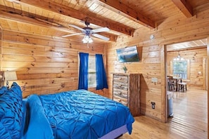 A wooden cabin room with a bed, a ceiling fan, a TV, and a view of the outdoors.