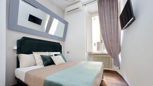 Ein Schlafzimmer mit einem Bett, einem großen Spiegel, einer Klimaanlage, einem Fernseher und einem Fenster mit Vorhängen.