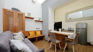 Ein kompakter Wohnbereich mit einer Couch, einem Esstisch, Stühlen, einer Küchenzeile mit Kühlschrank und einer Holzkabine mit Dekorationselementen.