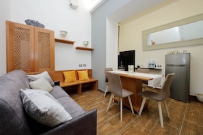 Um espaço compacto com sofá, mesa de jantar, cadeiras, cozinha equipada com geladeira e um armário de madeira com objetos decorativos.