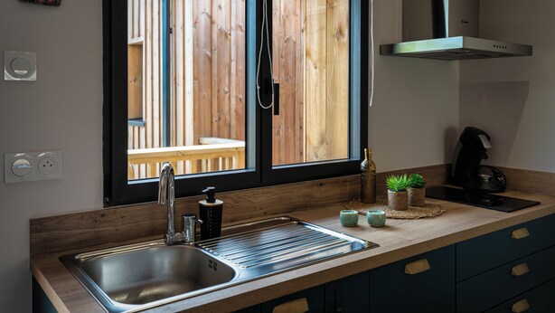 Une cuisine moderne dotée d’un évier en acier inoxydable, d’un plan de travail en bois et offrant une vue sur une terrasse en bois grâce à une grande fenêtre.
