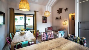 Un coin repas avec une table et des chaises en bois, un luminaire suspendu et une vue sur l’extérieur grâce à une grande fenêtre.