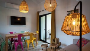 Un salon moderne avec une table à manger en bois, des chaises colorées, un canapé et deux lampes suspendues en osier.