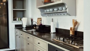 A modern kitchen with a stainless steel refrigerator, a built-in oven, a stovetop, and a large island with a sink. There are three pendant lights above the island, and a shelf above the countertop. - Amazing apartment in the best location! (תל אביב-יפו)
