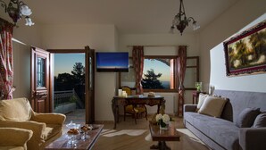 Una sala de estar con sofá, sillón, mesa de centro y televisor. Se aprecia una mesa de comedor con sillas y una ventana con cortinas.