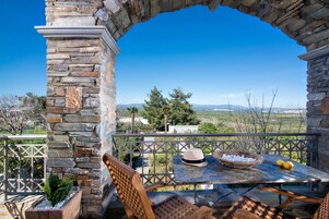 Un patio al aire libre con paredes de piedra, una mesa con sillas, un sombrero, limones y una cesta con hielo.