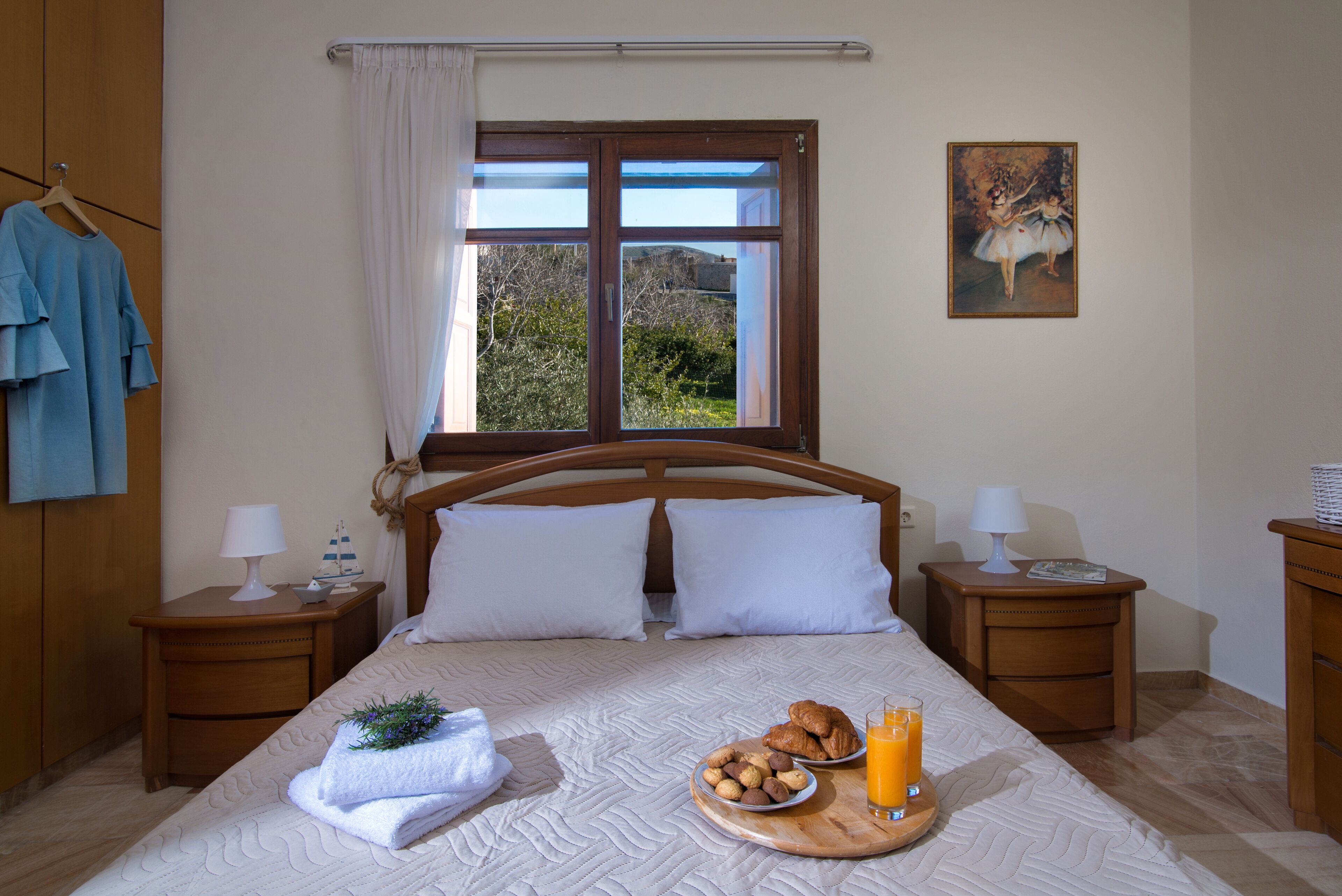 Una cama bien hecha con almohadas, una bandeja con croissants y jugo, y un cuadro en la pared.