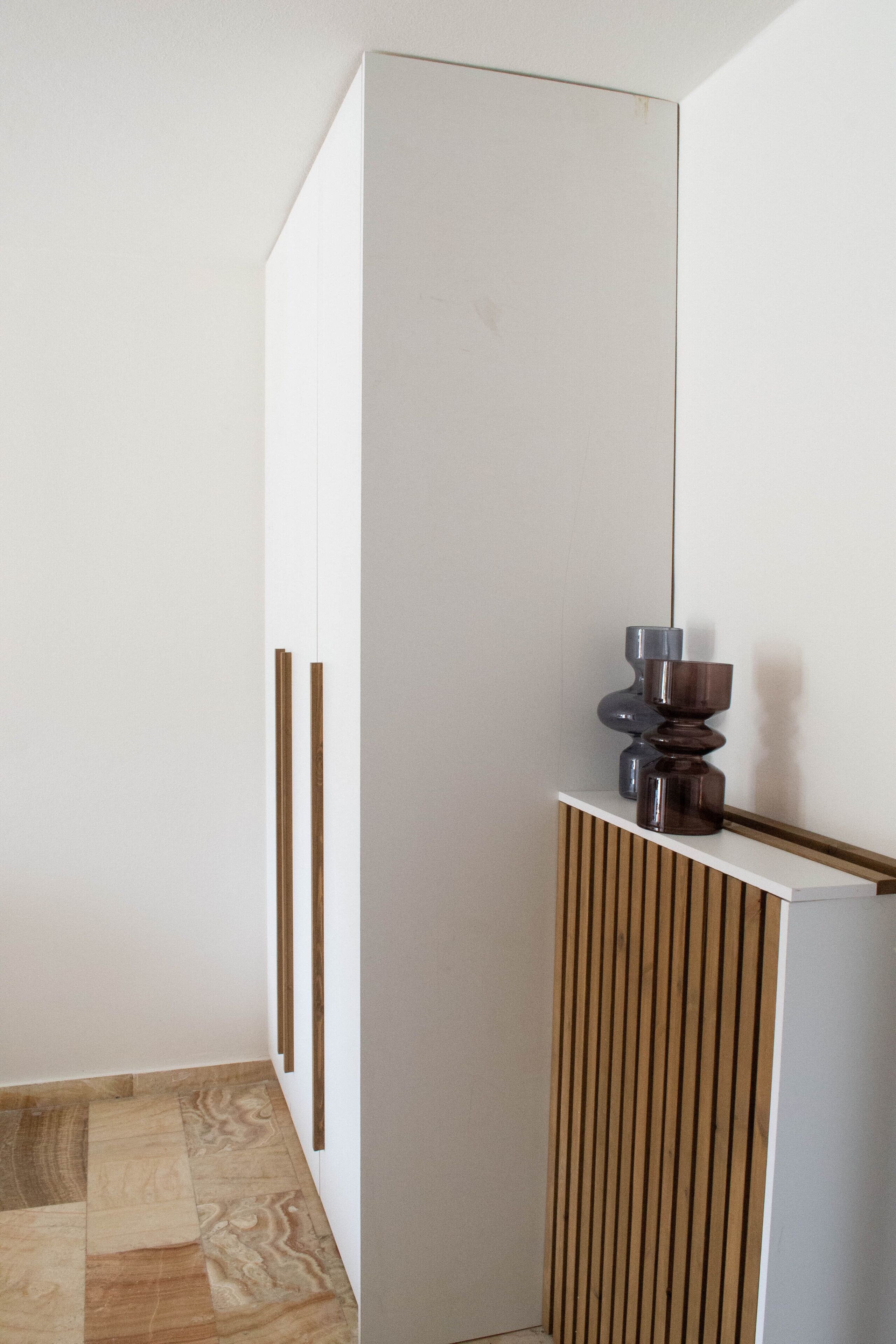 A minimalist room with a white wardrobe, a wooden panel, and a small table with a vase.