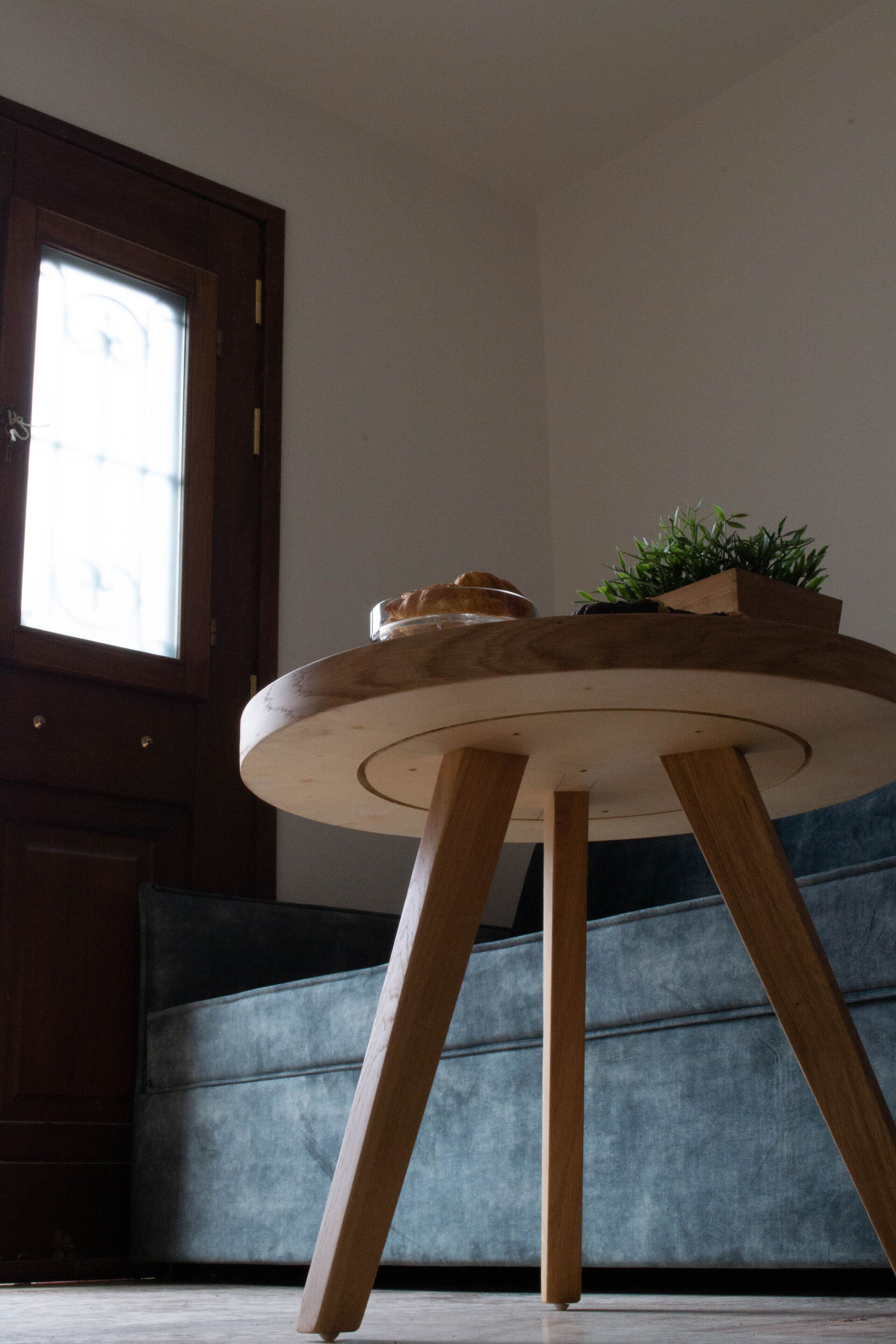 A round wooden table with a plant on top, placed in a room with a dark blue sofa and a wooden door.