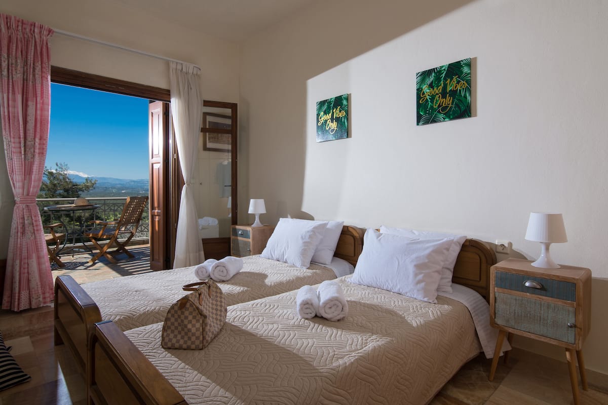 A hotel room with two beds, a balcony with a view, and a painting on the wall.