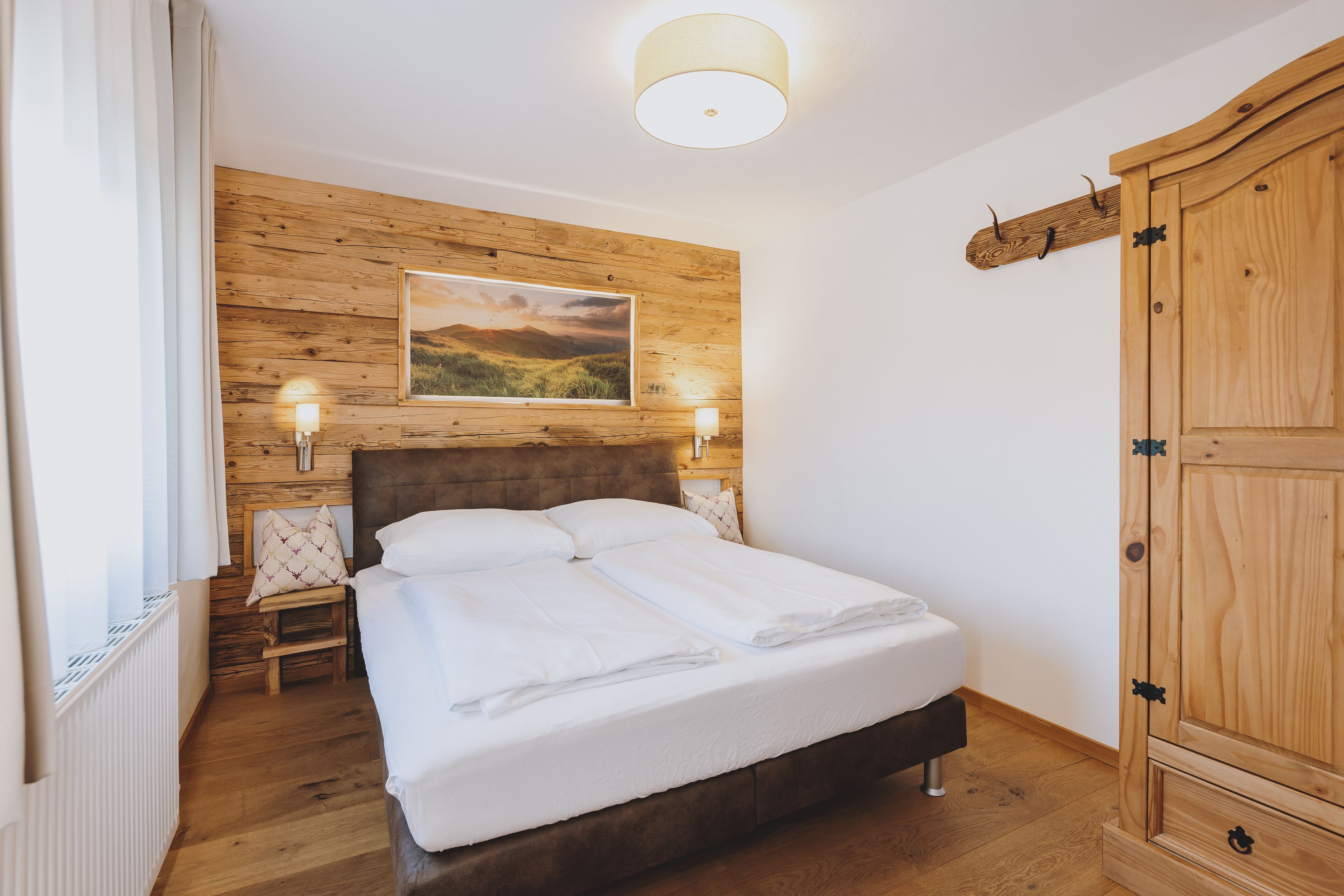 Un dormitorio con cabecera de madera, una cama grande con ropa blanca, dos lámparas de noche, un armario de madera y un cuadro con paisaje en la pared.