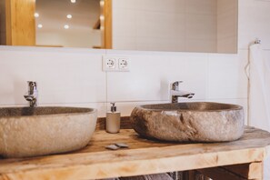 Ein Badezimmer mit zwei steinernen Waschbecken, einer Holz-Arbeitsplatte und einem Spiegel darüber.