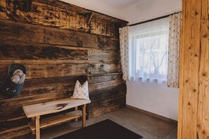 Ein rustikaler Raum mit einer Holzwand, einer Bank, einem Fenster mit gemusterten Vorhängen und einem Paar Hausschuhen auf dem Boden.