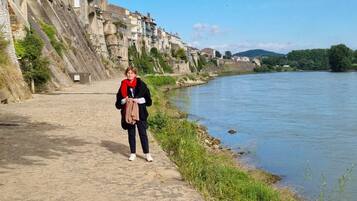 A person walking along a riverside path with buildings on the left and a river on the right.
