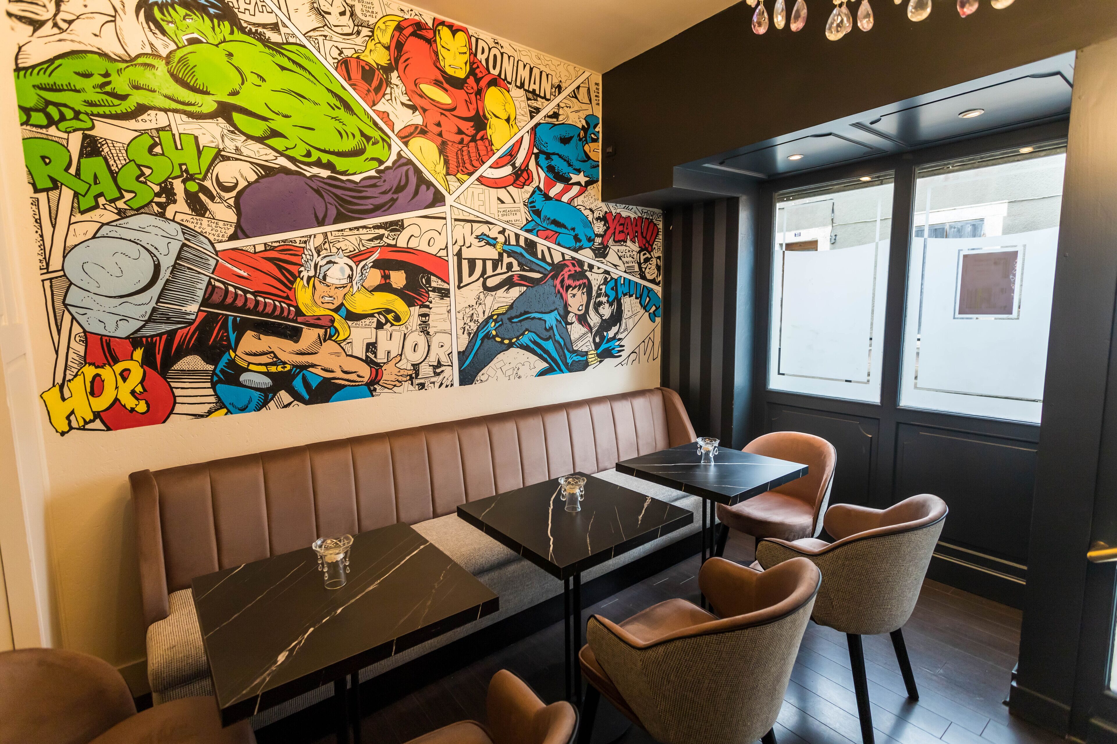 Interior de restaurante con un mural de estilo cómic, asientos de cuero y mesas de mármol negro.
