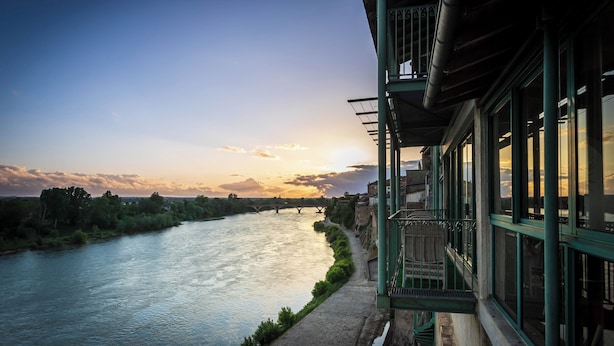 A riverside view with a bridge, a pathway, and a building with large windows and a balcony. - Côté Garonne-Le balcon des dames (Tonneins)
