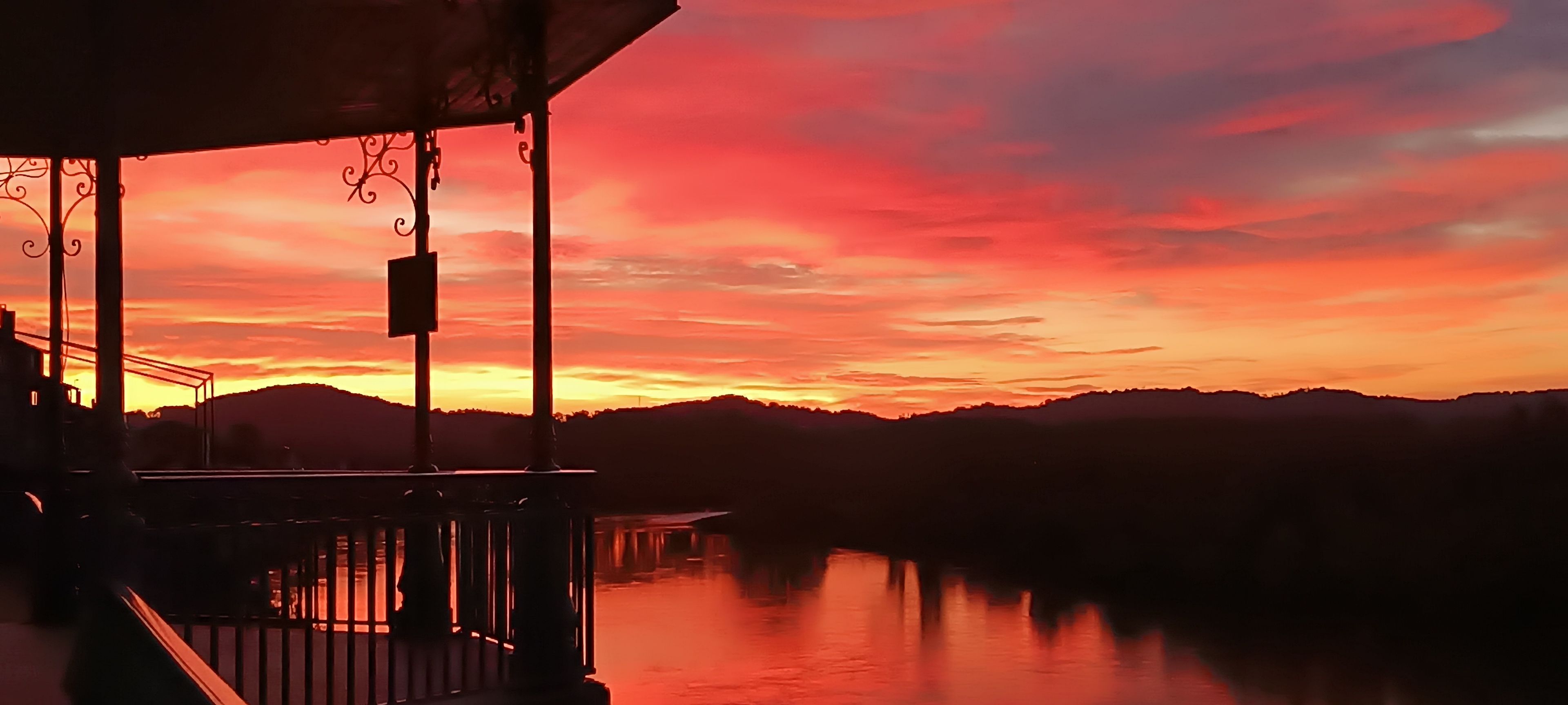 A sunset view from a balcony overlooking a body of water with distant hills.