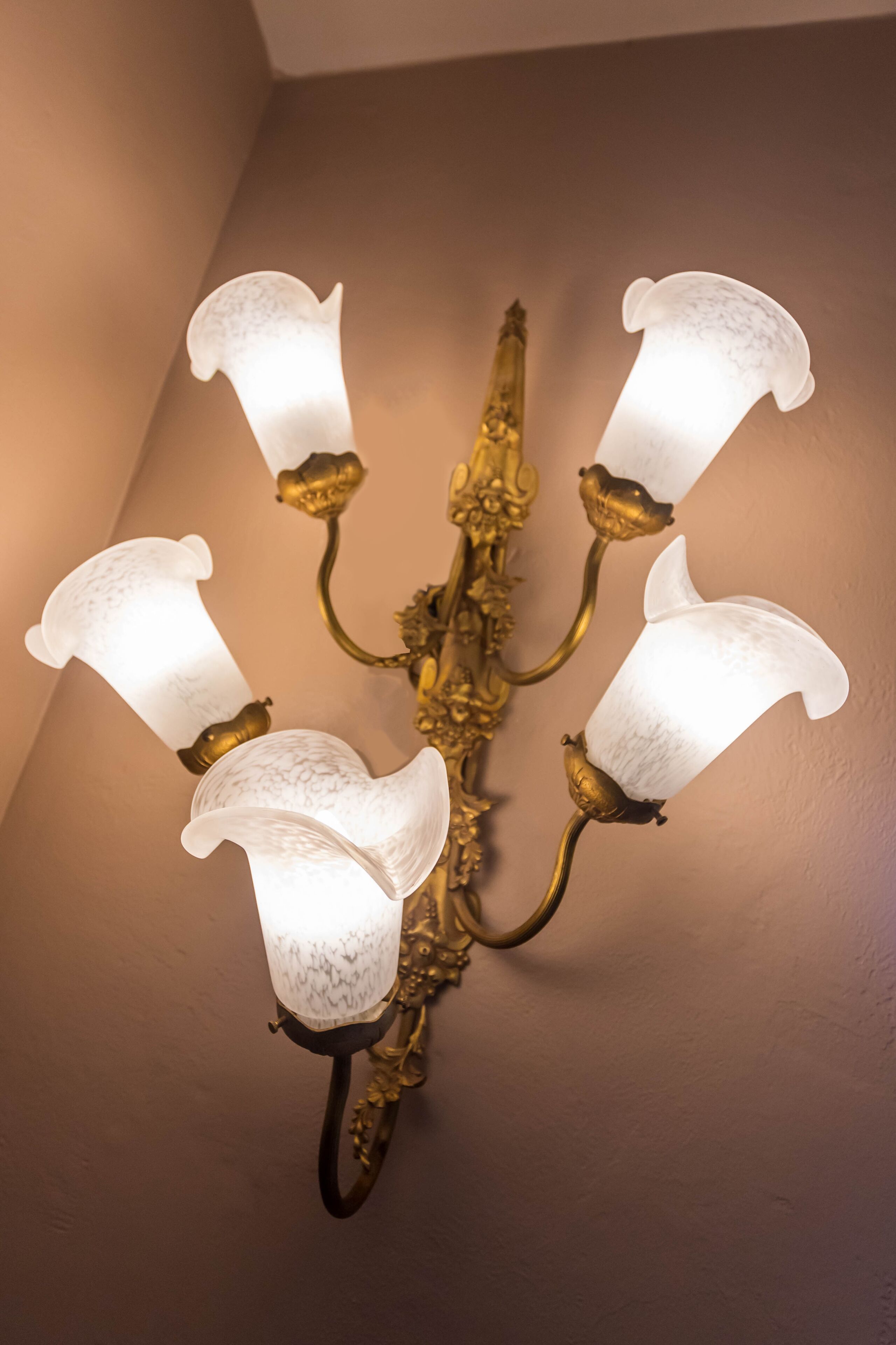 A wall-mounted chandelier with four glass shades and ornate metal fixtures.
