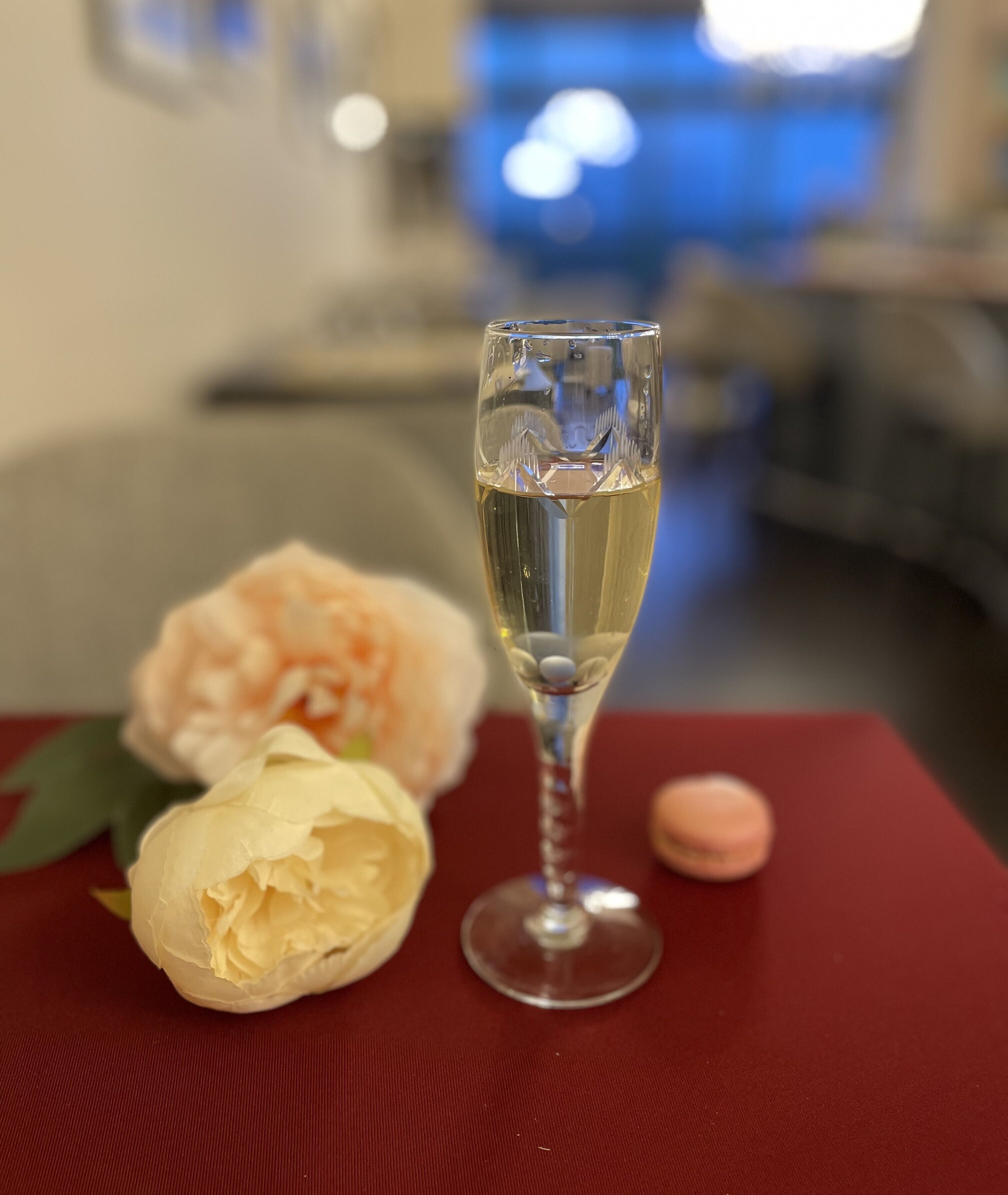 Un verre de champagne sur une table rouge, avec une fleur et un macaron.
