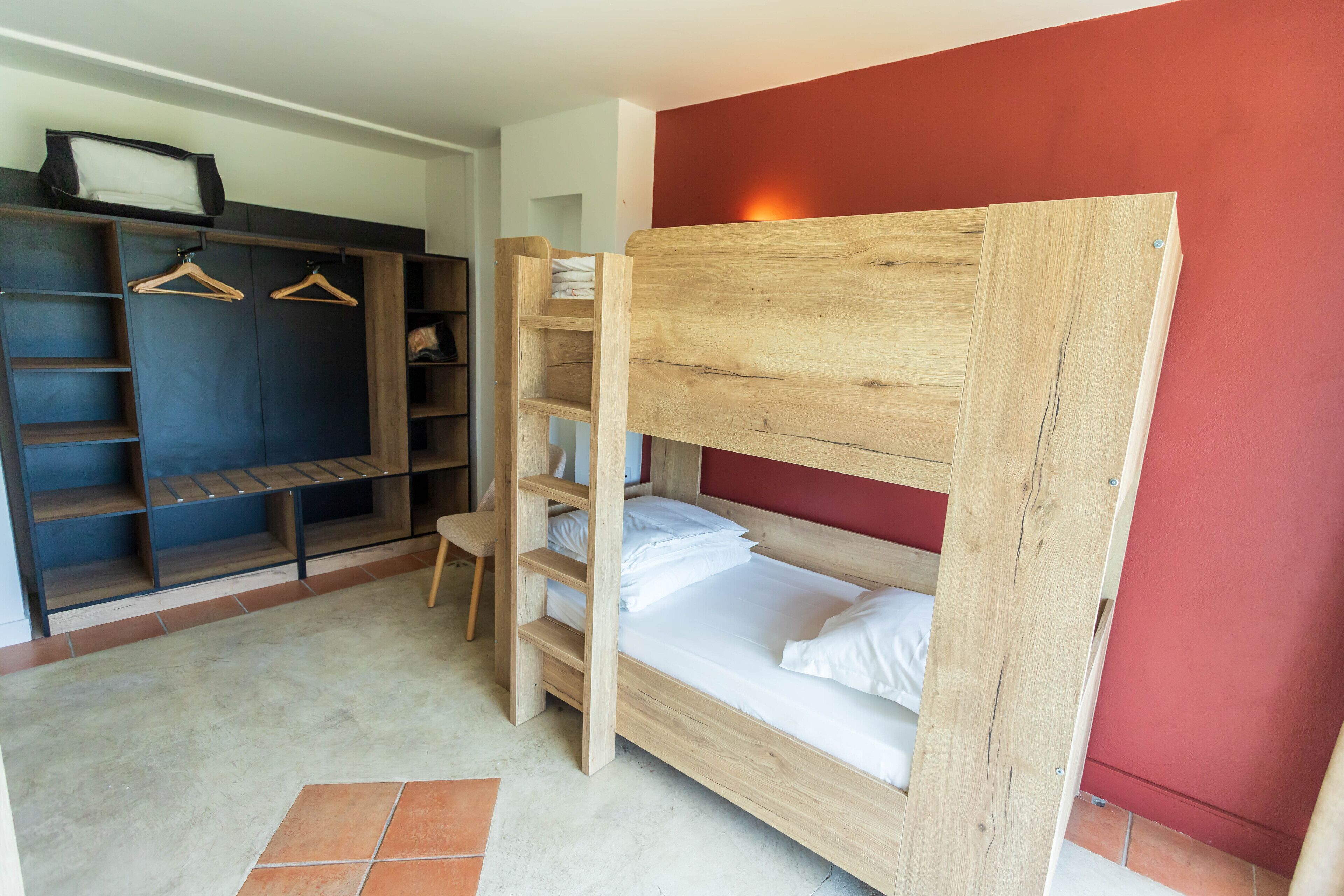 Een stapelbed met een houten hoofdbord, een kledingkast met hangruimte, en een betegelde vloer.