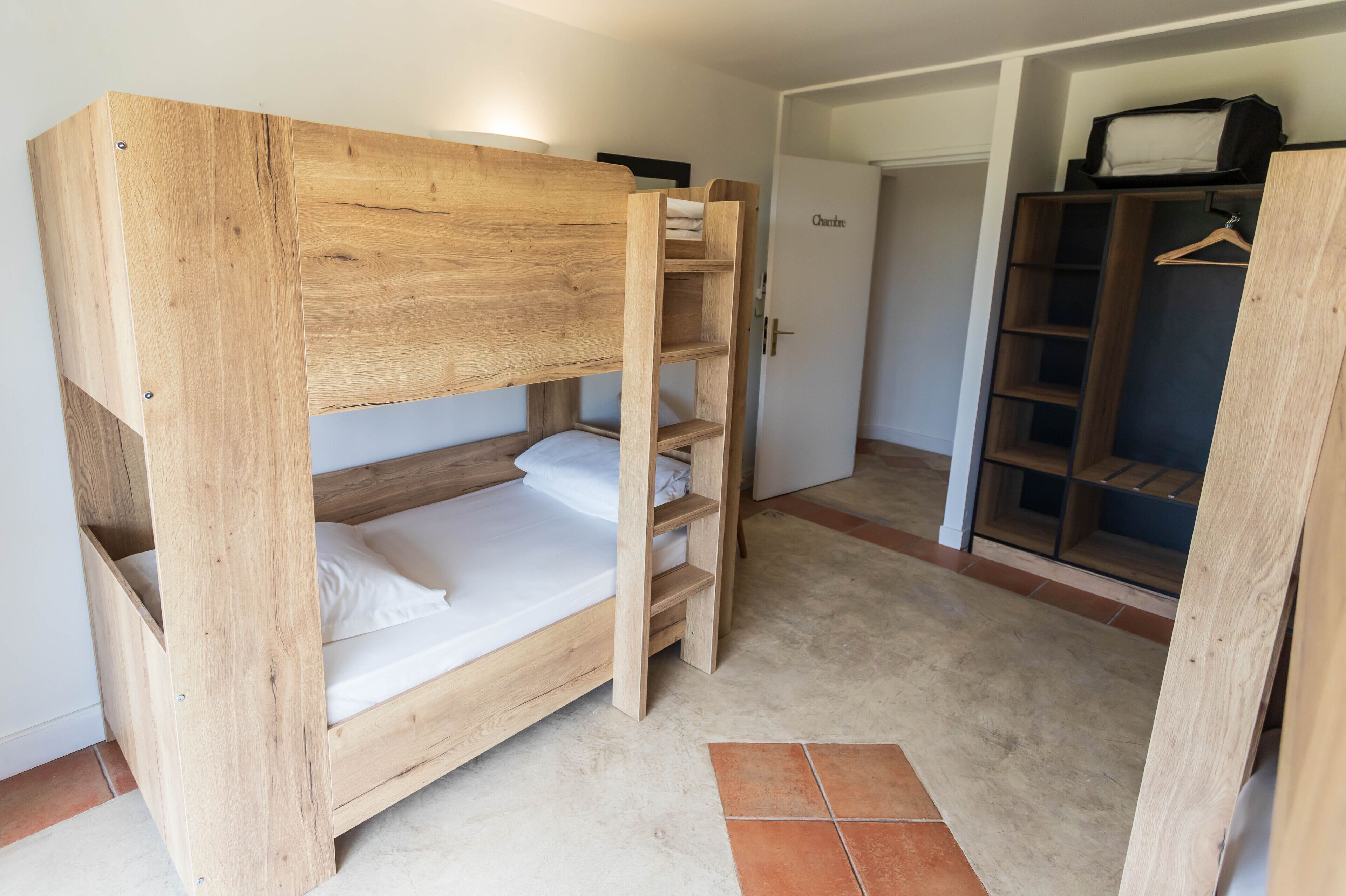 A bunk bed with a wooden frame and a wardrobe with open doors.