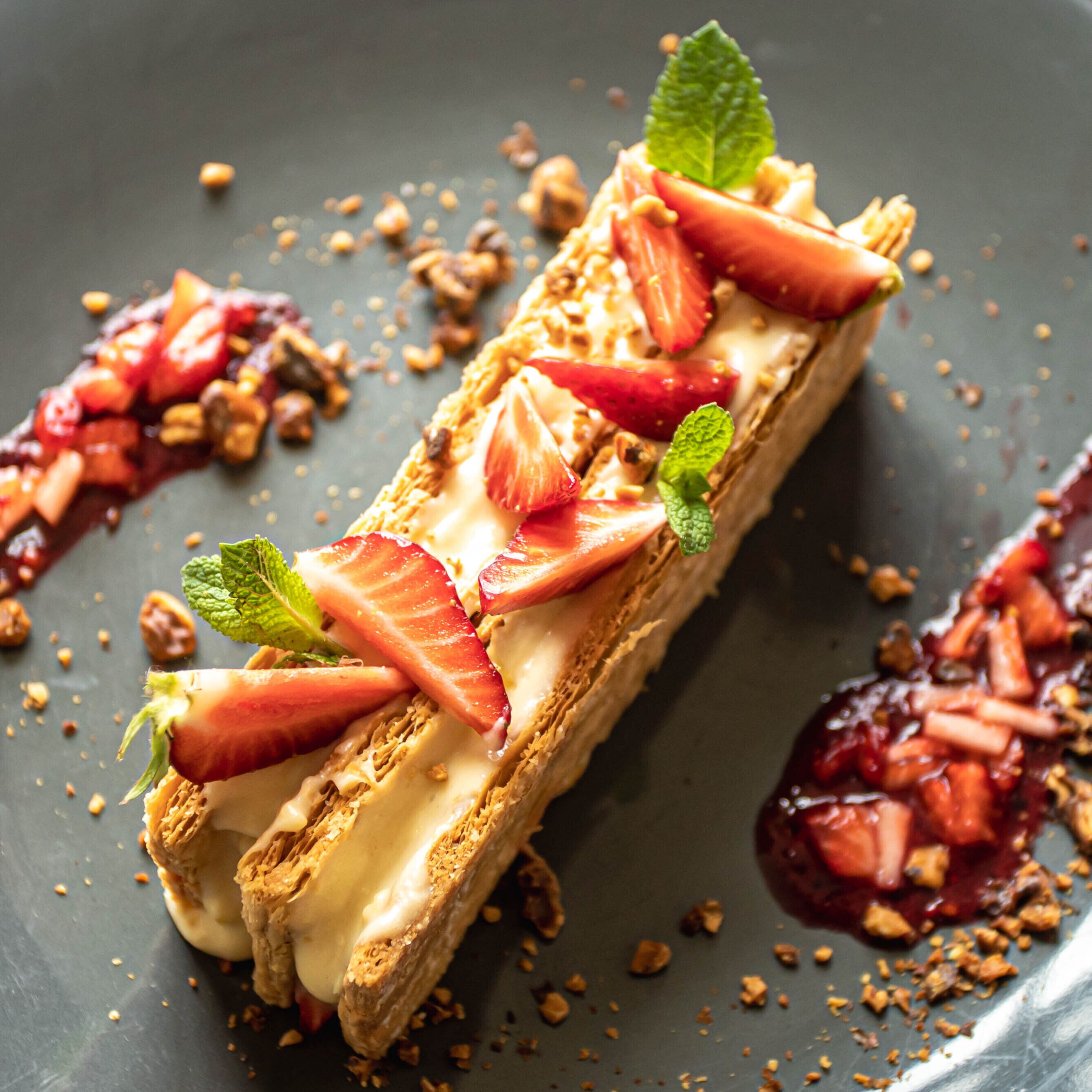 A dessert with strawberries and mint leaves on a dark plate.