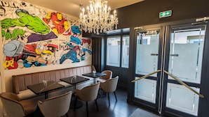 A restaurant with a mural of comic book characters, a chandelier, and a glass door entrance. - Côté Garonne-Le balcon des dames (Tonneins)