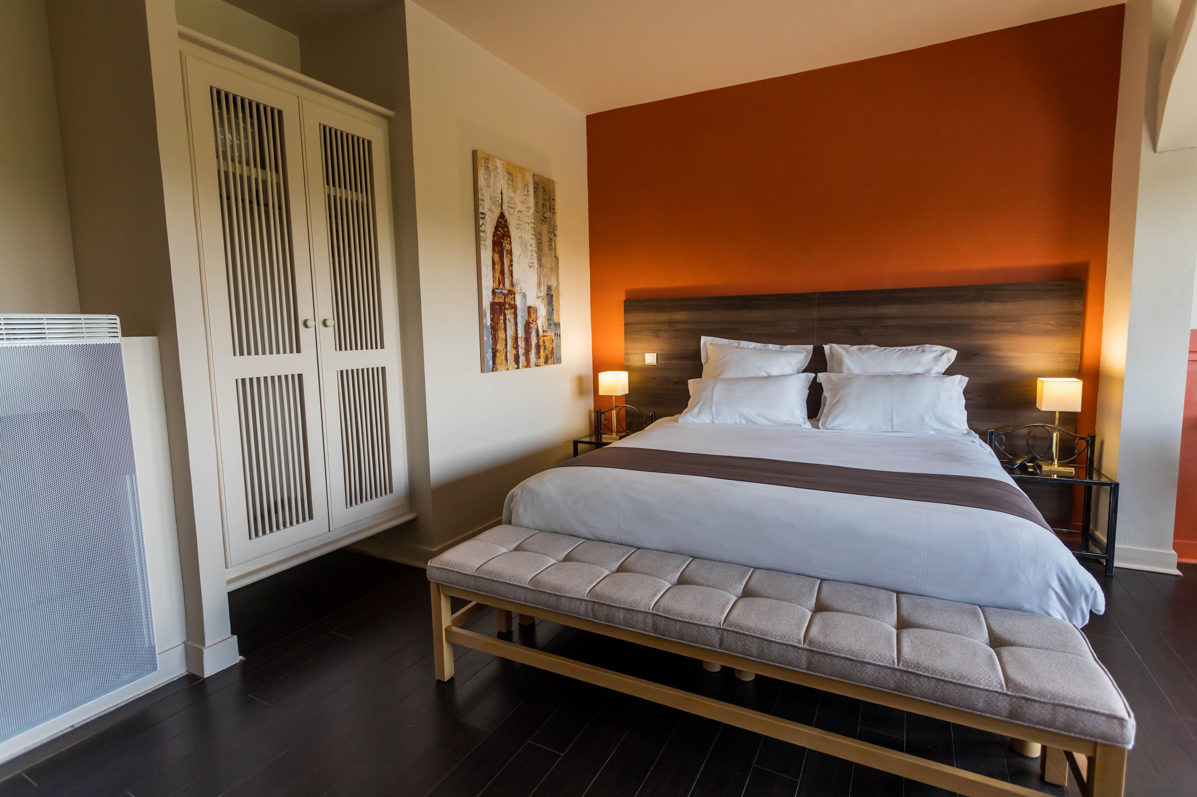 A hotel room with a large bed, a bench, a wardrobe, and a wall-mounted artwork.
