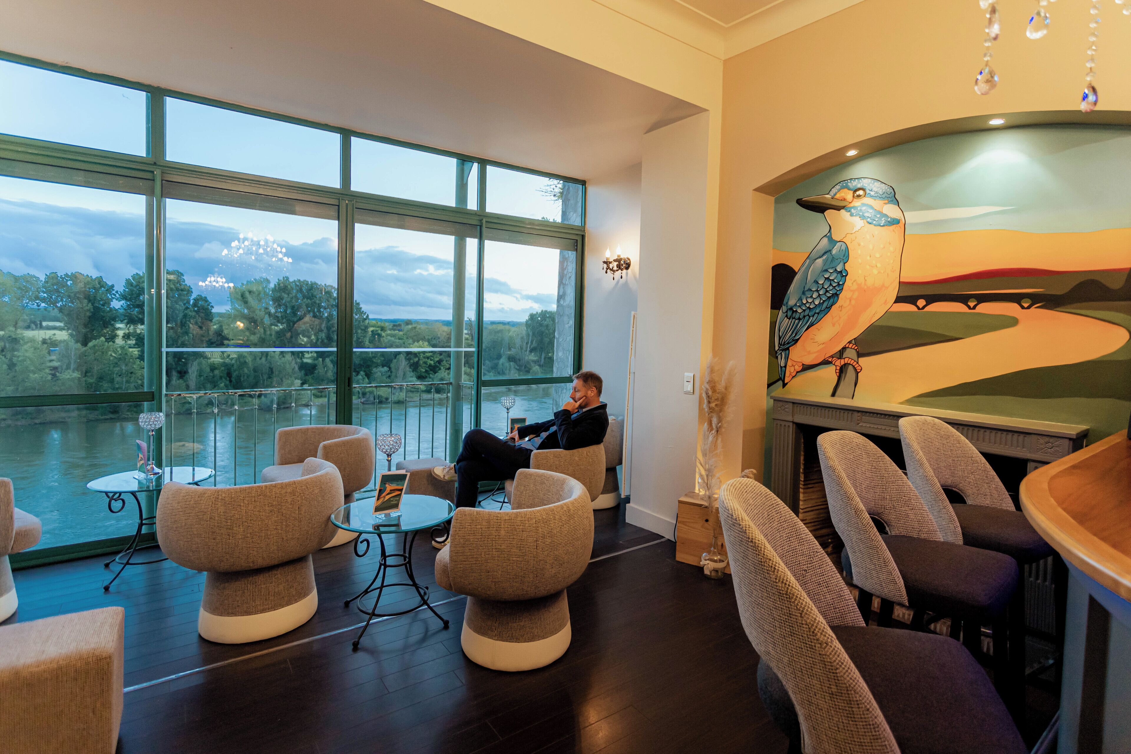 Un salón moderno con ventanas amplias, asientos cómodos y un mural de un ave.
