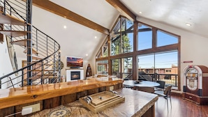 A spacious loft with a wooden staircase, a fireplace, a large window, and a jukebox.