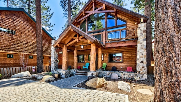 A log cabin with a covered porch, stone foundation, and multiple windows.