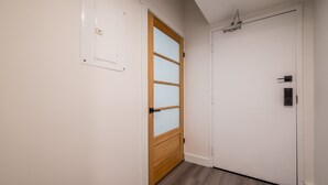 Un pasillo con una puerta de madera con paneles de vidrio satinado, una puerta blanca con manija y un interruptor de luz en la pared.