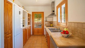 A kitchen with wooden cabinets, a white refrigerator, a double sink, and a window with a view. - SES SAVINES A charming, peaceful house with a pool and BBQ, 2km from the beach (Illes Balears)