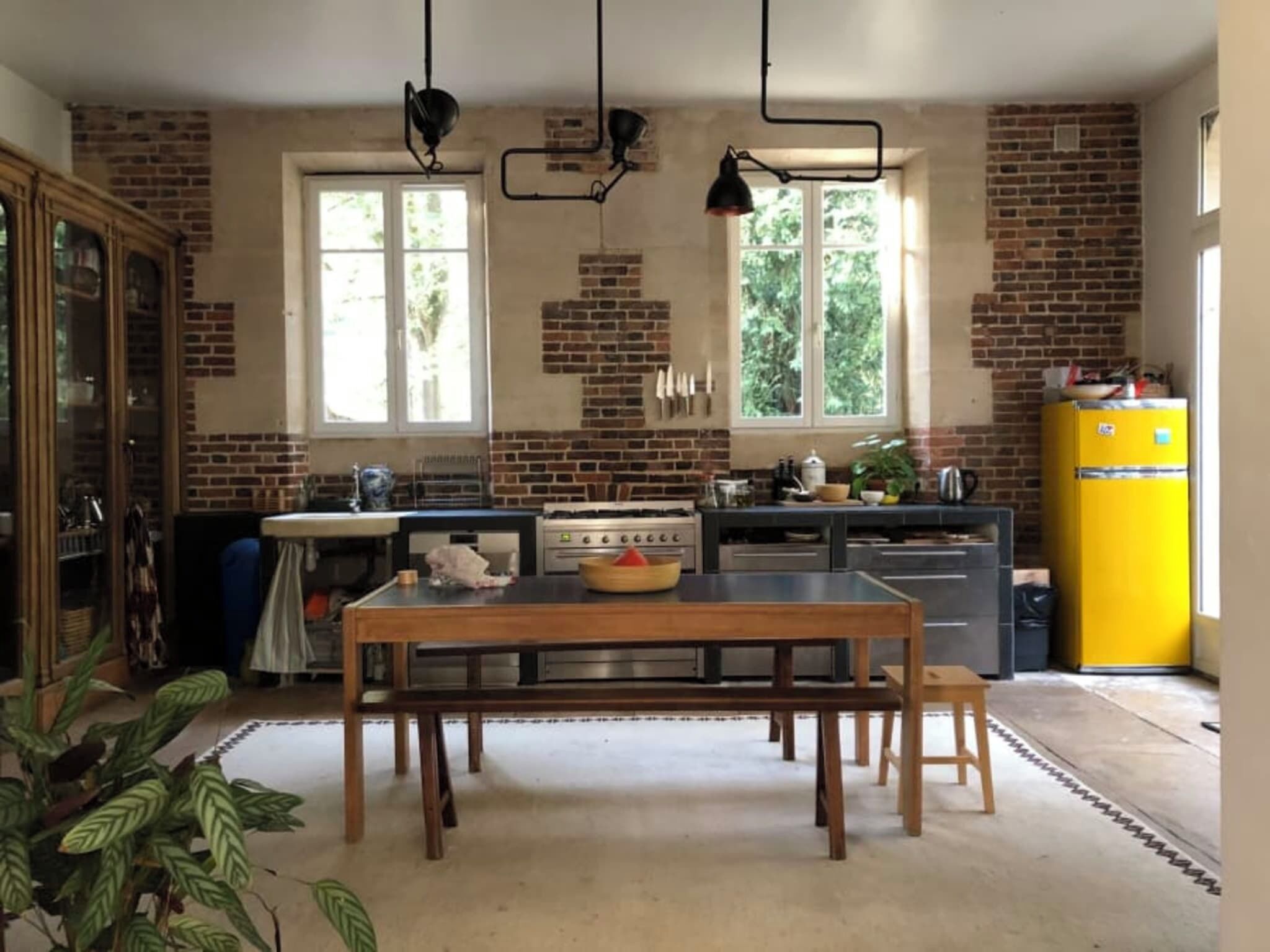 A kitchen with a wooden table, a yellow refrigerator, and a brick wall.