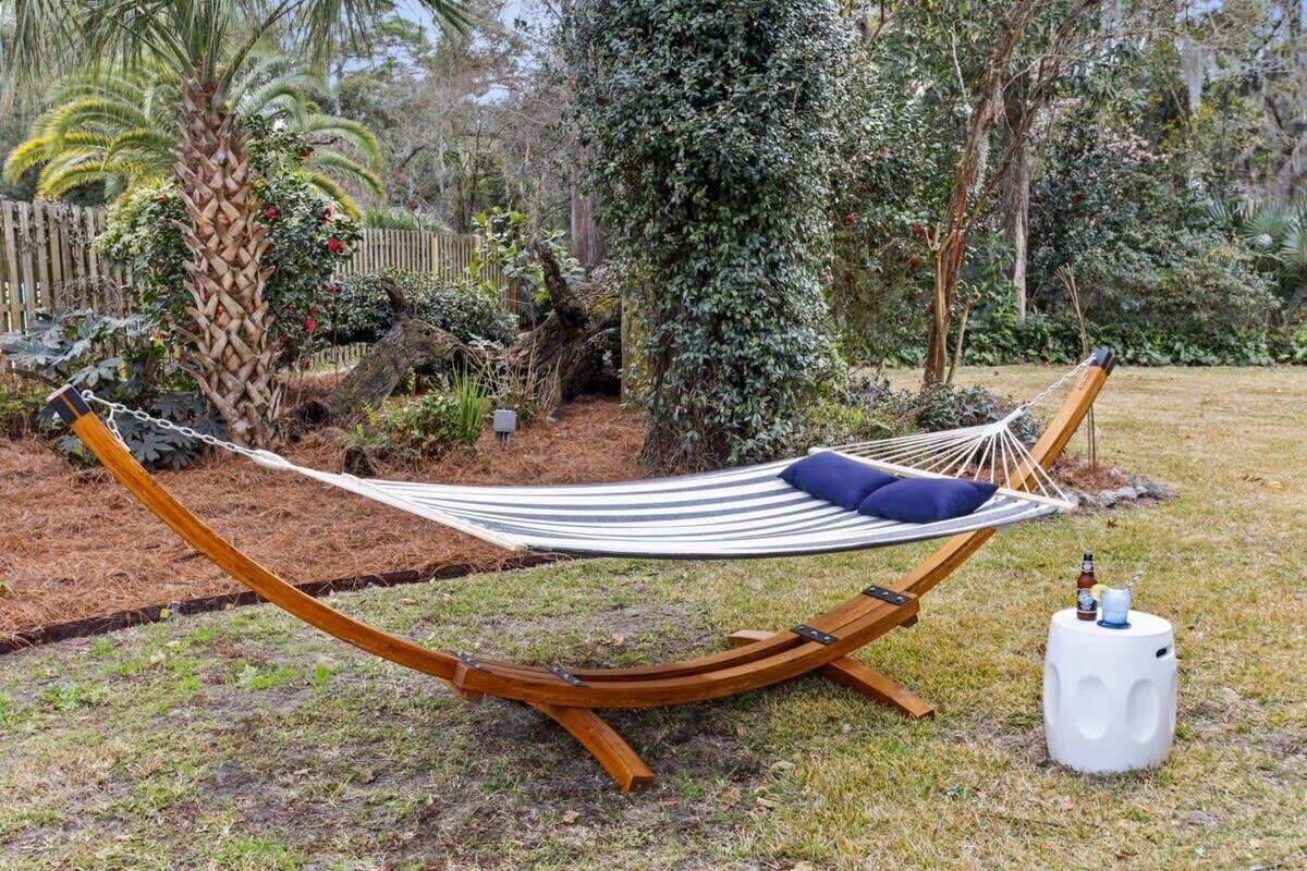A hammock with a wooden frame and a white and black striped fabric, placed on grass with a small white stool nearby.